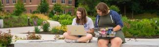 Two students on their laptops sitting outside on the Biddeford Campus